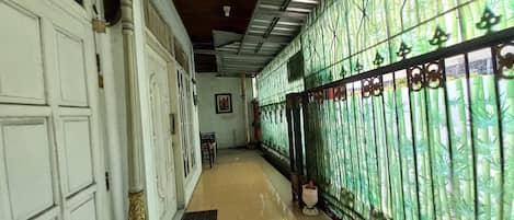 A corridor with a tiled floor, a white door on the left, and a green bamboo-patterned gate on the right.