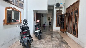 Un couloir étroit où sont garées deux motos, un miroir sur le côté gauche et une fenêtre avec un ventilateur sur le côté droit.