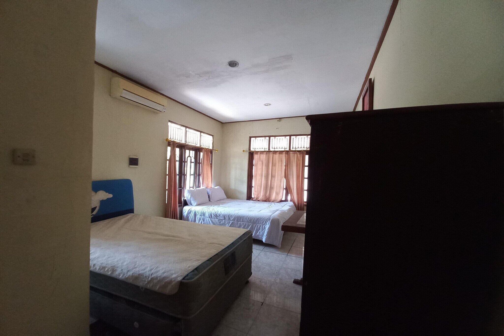 A room with two beds, a window with curtains, and an air conditioning unit.