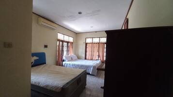 A room with two beds, a window with curtains, and an air conditioning unit.