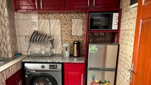 A compact kitchen with a washing machine, a microwave, and a refrigerator. - Comfy Cityscape Elegance (Yaoundé)