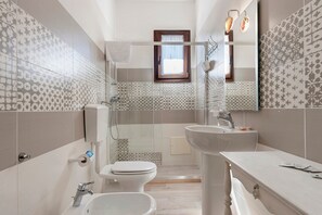 A bathroom with a toilet, bidet, and sink, featuring patterned tiles and a window. - Camera Mora - 3 Guests - (Porto Cesareo)