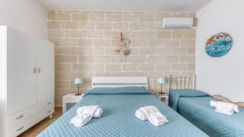 A bedroom with a brick wall, a white wardrobe, two beds with blue bedding, and a wall-mounted air conditioner.