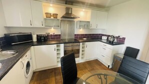 A compact kitchen with a washing machine, a coffee maker, and a microwave. - SeaBeach View Coastal Path Ground Floor Apartment (LLANELLI)