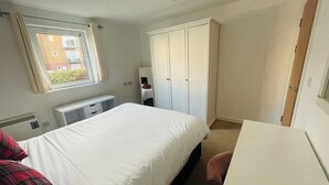 A bedroom with a bed, a desk, a wardrobe, and a window. - SeaBeach View Coastal Path Ground Floor Apartment (LLANELLI)