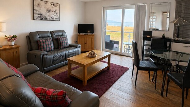 A living room with a sofa, a coffee table, a TV, and a dining area with a table and chairs. - SeaBeach View Coastal Path Ground Floor Apartment (LLANELLI)