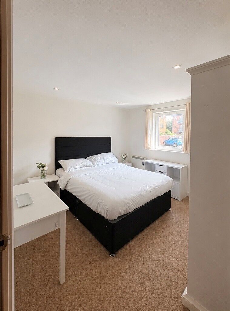 A bedroom with a bed, bedside tables, a desk, and a window.