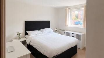 A bedroom with a bed, bedside tables, a desk, and a window.