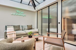 A modern living room with a sofa, armchairs, a coffee table, and a glass door leading to a balcony. - Sublim Apartment - Le Marais - Beaubourg (Paris)