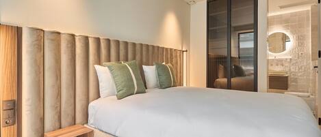 Un dormitorio moderno con una cama grande, una mesita de noche de madera y una puerta corrediza de vidrio que da al baño.