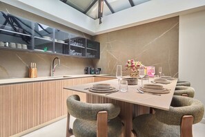 A modern kitchen with a built-in island, a dining area with a long table, and a seating arrangement with upholstered chairs. - Sublim Apartment - Le Marais - Beaubourg (Paris)