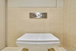 Eine Toilette in einem Badezimmer mit beige gefliesten Wänden und einem Spülhebel.