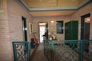 A hallway with brick walls, green doors, and a metal railing. - Apartment in Verbania near Lake and Islands (Verbania)