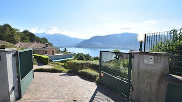 A paved pathway leading to a gated entrance with a view of a lake and mountains in the background.
