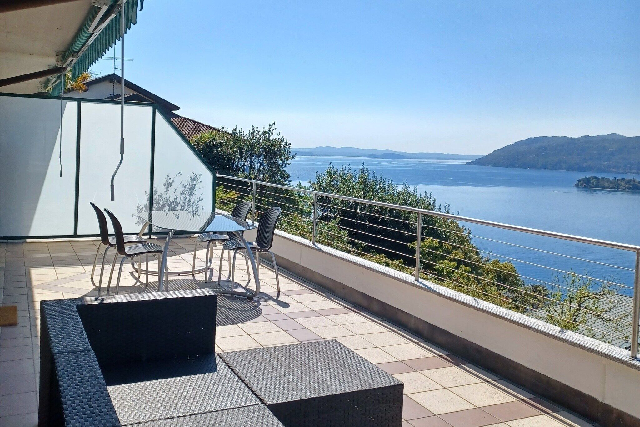 Un balcon avec vue sur un lac et des montagnes, aménagé avec des chaises et une table.