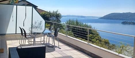 Un balcón con vistas a un lago y montañas, amoblado con sillas y una mesa.