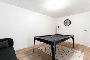 Ein Zimmer mit Billardtisch, Wanduhr und Sofa.