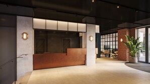 A reception area with a wooden reception desk, two wall-mounted light fixtures, and a potted plant. - Student Only Ark Canning Town (London)