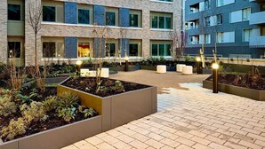 A multi-story residential building with a courtyard featuring planters and seating areas. - Student Only Ark Canning Town (London)