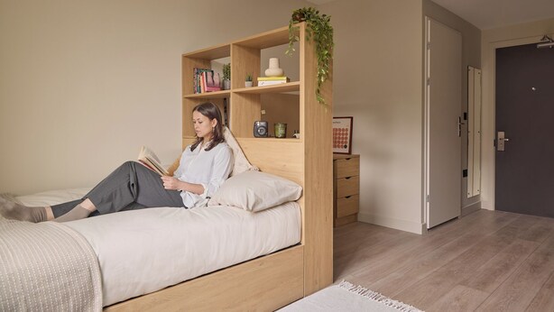 A bedroom with a bed, a wooden bookshelf, and a door. - Student Only Ark Canning Town (London)