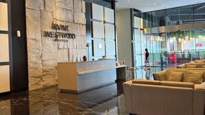 Een hotellobby met een receptiebalie, een stenen muur met de naam van het hotel, een zithoek en een glazen ingang.