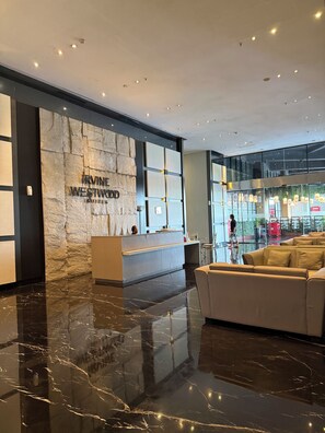 Eine Hotelhalle mit einer Rezeption, einer Wand aus Stein mit dem Namen des Hotels, einer Sitzecke und einem Glastür-Eingang.
