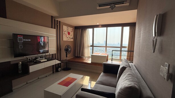 Een moderne woonkamer met een flatscreen televisie, een bank, een salontafel en een groot raam met uitzicht op de stad.