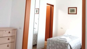 Um quarto com um guarda-roupa de madeira, uma cama com colcha estampada e um espelho refletindo uma porta e um quadro na parede.