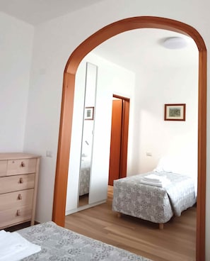 Ein Schlafzimmer mit einem Holzschrank, einem Bett mit gemustertem Überwurf und einem Spiegel, der eine Tür und ein gerahmtes Bild an der Wand reflektiert.