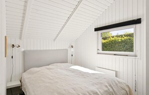 A bedroom with a sloped ceiling, a window with a view of greenery, and a bed with a white bedspread. - 3 bedroom lovely home in Dronningmølle (Dronningmølle)