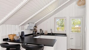 A kitchen with a black countertop, white cabinets, and a door with a window. There are two black bar stools and a woven basket on the counter.