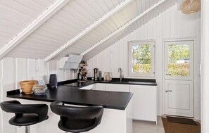 A kitchen with a black countertop, white cabinets, and a door with a window. There are two black bar stools and a woven basket on the counter. - 3 bedroom lovely home in Dronningmølle (Dronningmølle)