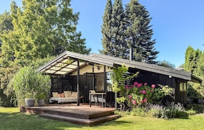 A modern outdoor seating area with a table and chairs, surrounded by lush greenery and flowering plants. - 2 bedroom gorgeous home in Gilleleje (Gilleleje)