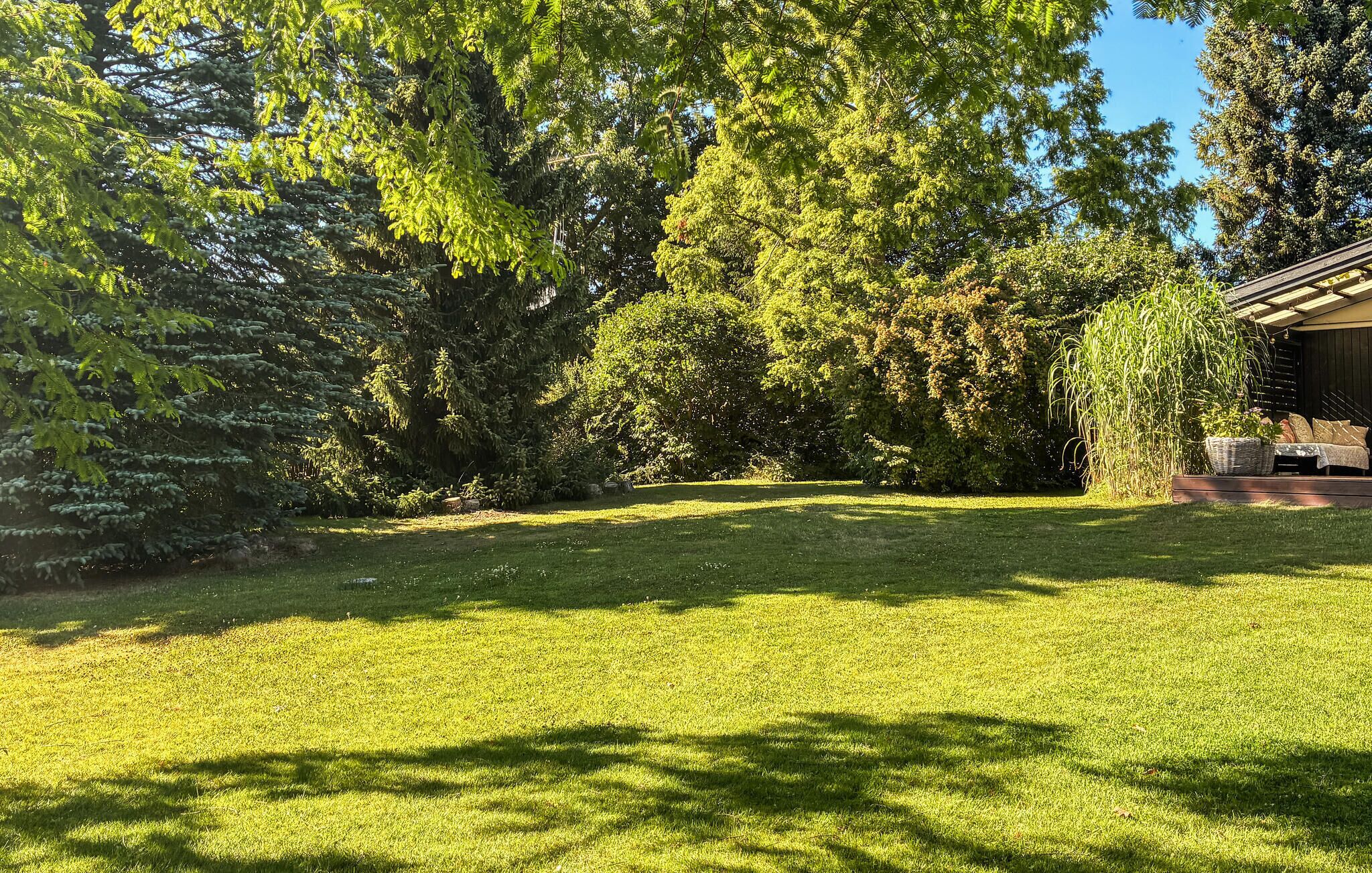 Une pelouse verdoyante et bien entretenue, agrémentée de divers arbres, et un bâtiment doté d’un toit en pente.