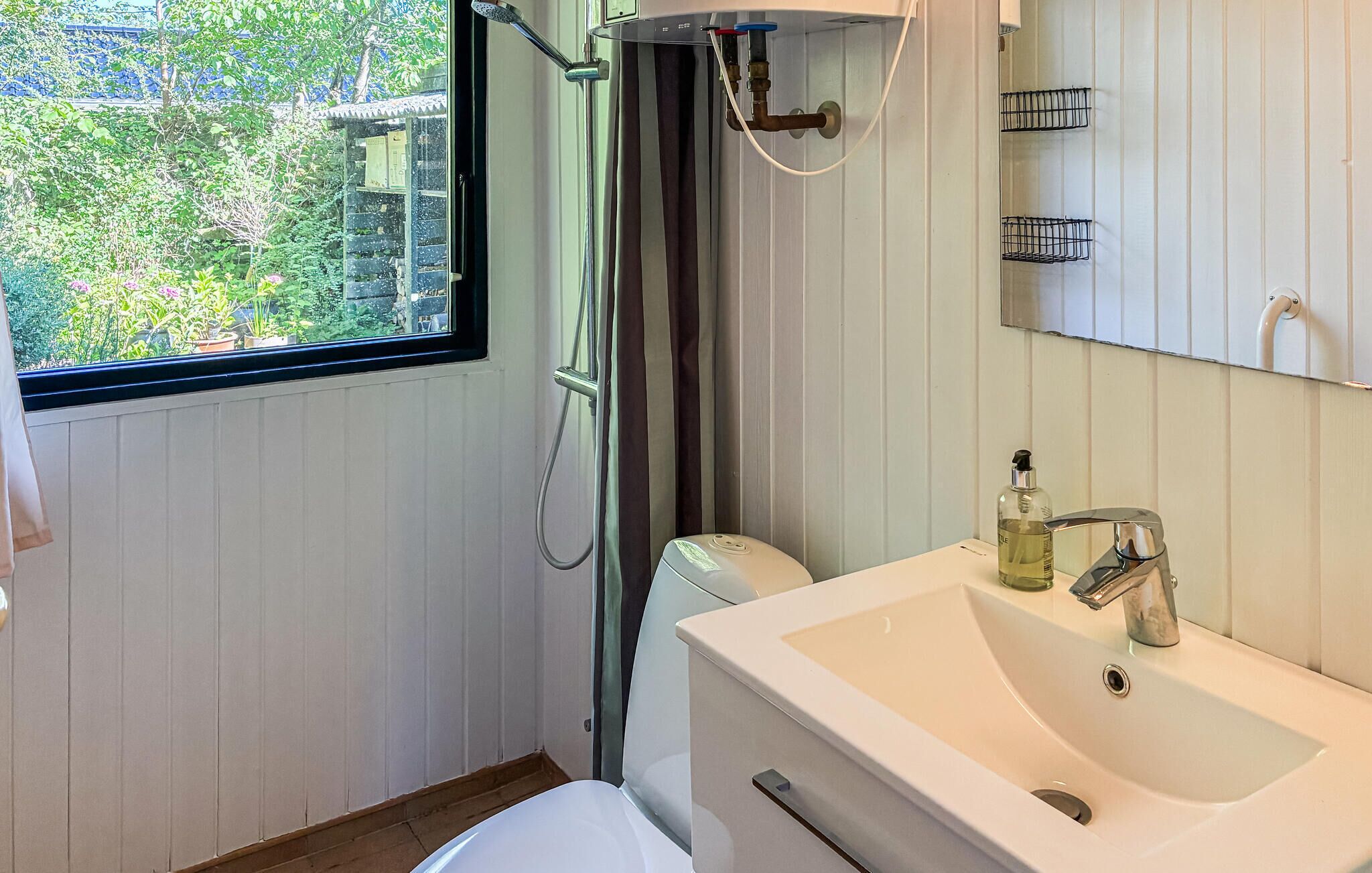 Een badkamer met een wit wastafelmeubel, een douche en een raam met uitzicht op groen.