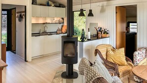 A modern kitchen with a central wood stove, a dining area with wicker furniture, and a view of the outdoors.