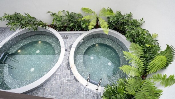 Duas banheiras de hidromassagem circulares com água cristalina, cercadas por vegetação exuberante.