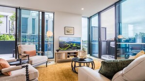 Uma sala de estar moderna com sofá, poltronas, mesa de centro, televisão e uma grande janela com vista para o exterior.