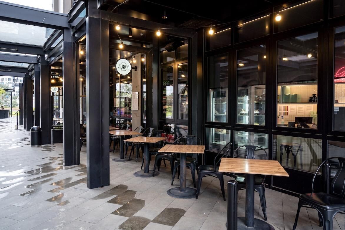 An outdoor cafe area with tables and chairs, a glass storefront, and a visible menu board.
