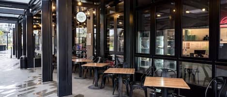 An outdoor cafe area with tables and chairs, a glass storefront, and a visible menu board.