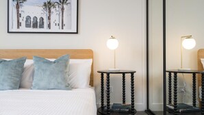Quarto de hotel com uma cama, duas mesas de cabeceira com luminárias, um quadro na parede e um espelho grande.