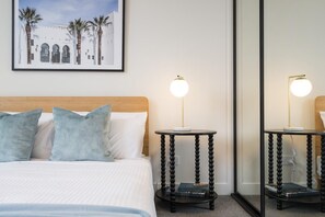 Ein Hotelzimmer mit einem Bett, zwei Nachttischen mit Lampen, einem gerahmten Bild an der Wand und einem großen Spiegel.