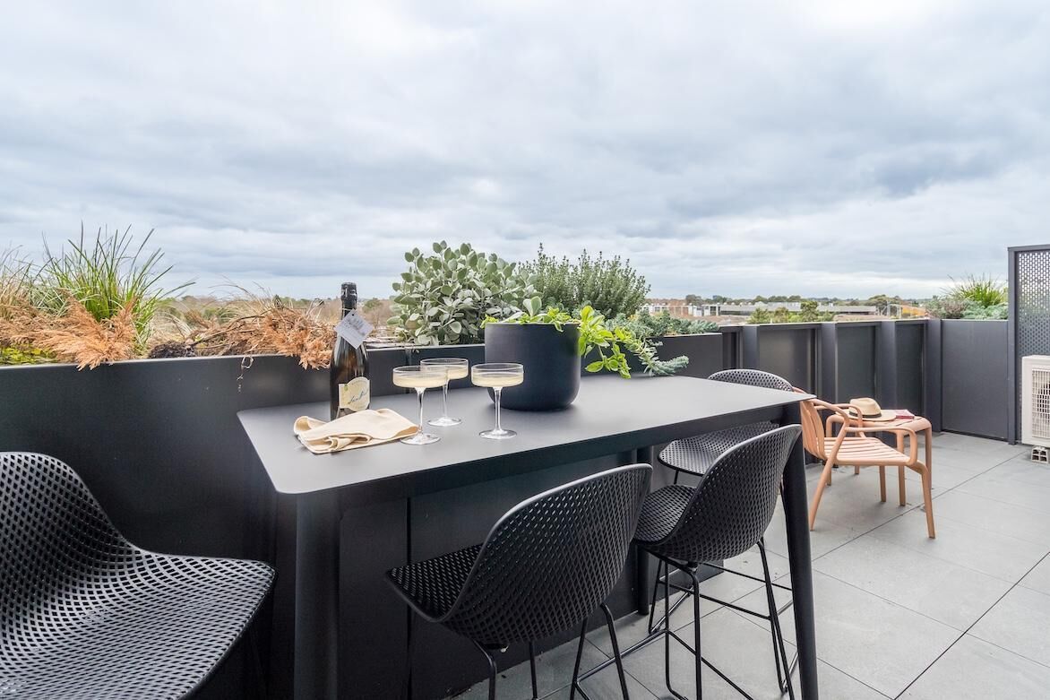 Terraza en la azotea con una mesa para dos, sillas negras, una planta en maceta y una botella de champán.