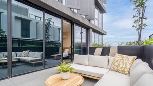 Uma área externa moderna com um sofá, uma mesa redonda de madeira e um vaso de planta.