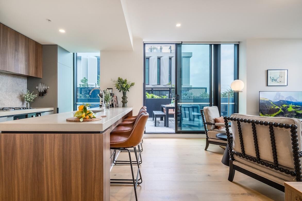 A modern kitchen with a central island, bar stools, and a dining area with a sofa and table.