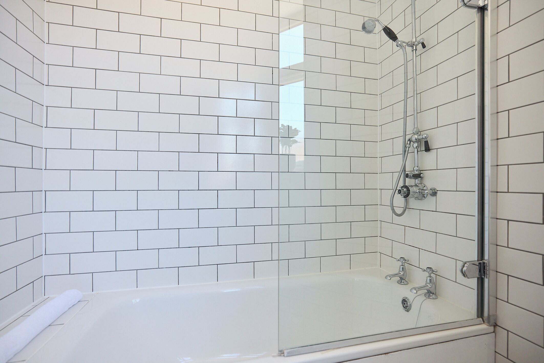A modern bathroom with white subway tiles, a glass-enclosed shower, and a white bathtub.