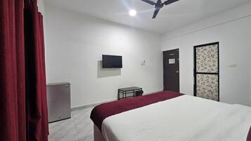 Una habitación con una cama, ventilador de techo, televisor, escritorio y armario.