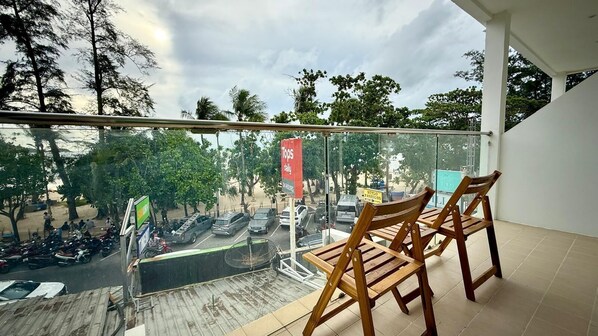 A balcony with a view of parked vehicles and trees, wooden chairs, and a glass railing. - Boutique 1BR Suite with Sea View, Patong (Tambon Patong)