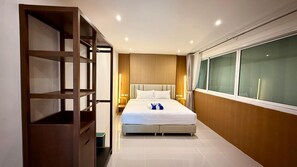 A hotel room with a bed, bedside tables, a wardrobe, and a large window. - Boutique 1BR Suite with Sea View, Patong (Tambon Patong)