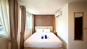 A hotel room with a bed, curtains, a headboard, an air conditioning unit, a nightstand, and a mirror.